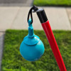 A Desert Blue roller ball tip with a hook-style attachment hangs from an Awarewolf Gear Urban Xplorer cane, which is red with a black grip. The background shows a sidewalk and grass, indicating an outdoor urban setting.