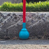A Desert Blue roller ball tip is attached to an Awarewolf Gear All Terrain Cane, shown making contact with a paved surface. The red cane and blue tip are in sharp focus, while the background is softly blurred, suggesting a suburban or urban outdoor environment. Slip on tip.