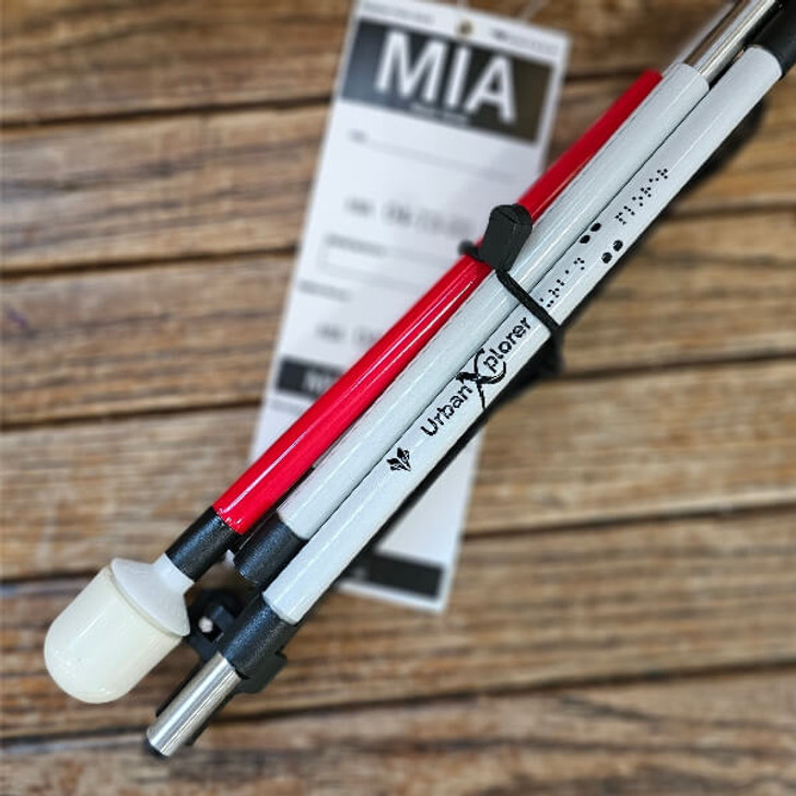 Urban Xplorer mobility cane folded up, sitting on a wooden bench with a checked bag tag for Miami.