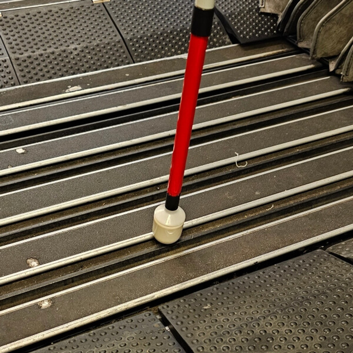 Urban Xplorer mobility cane fully extended with the dome tip cruising across metal and rubber planks in between two rail cars.