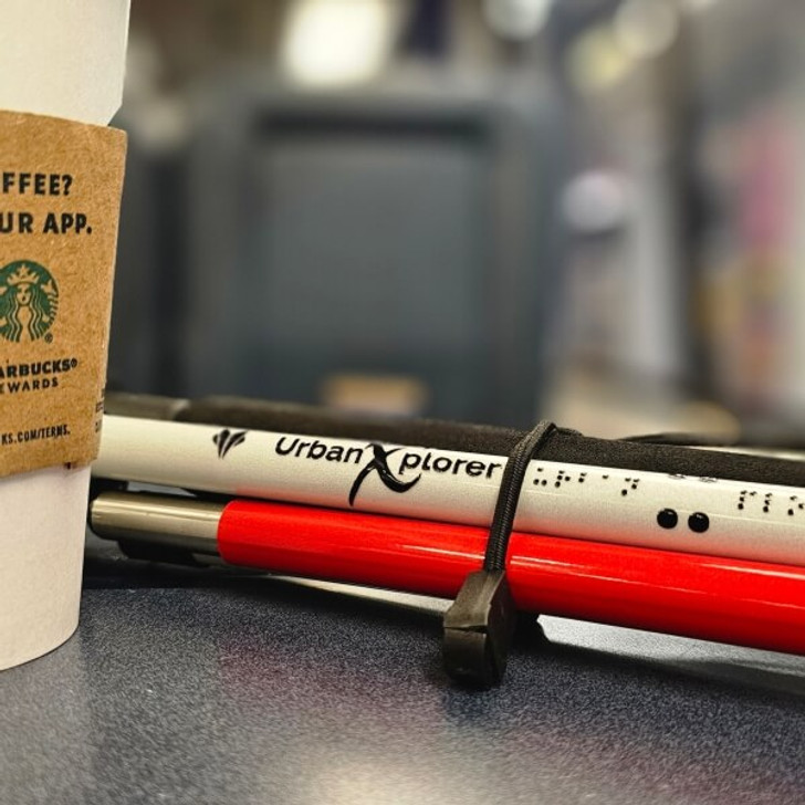 Urban Xplorer cane folded up and sitting next to a cup of coffee on a seatback tray onboard an Amtrak Acela train.