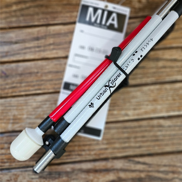 Urban Xplorer mobility cane folded up, sitting on a wooden bench with a checked bag tag for Miami.