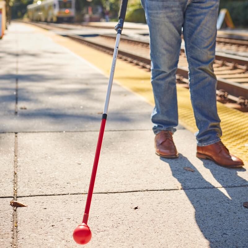 Male walking along a concrete railway platform with the All Terrain Cane in his right hand. 