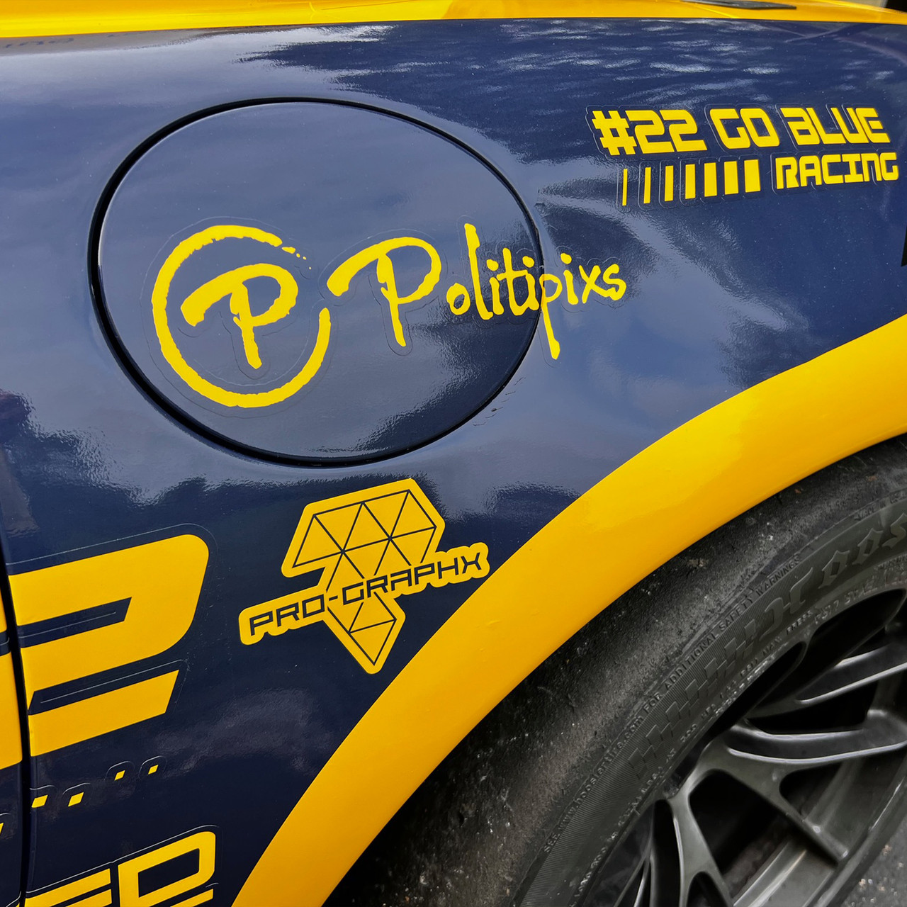 Close-up of a race car's rear panel featuring bold yellow decals on a glossy blue surface, including the logos for Politipixs and Pro-Graphx, along with “#22 Go Blue Racing” near the fuel cap.