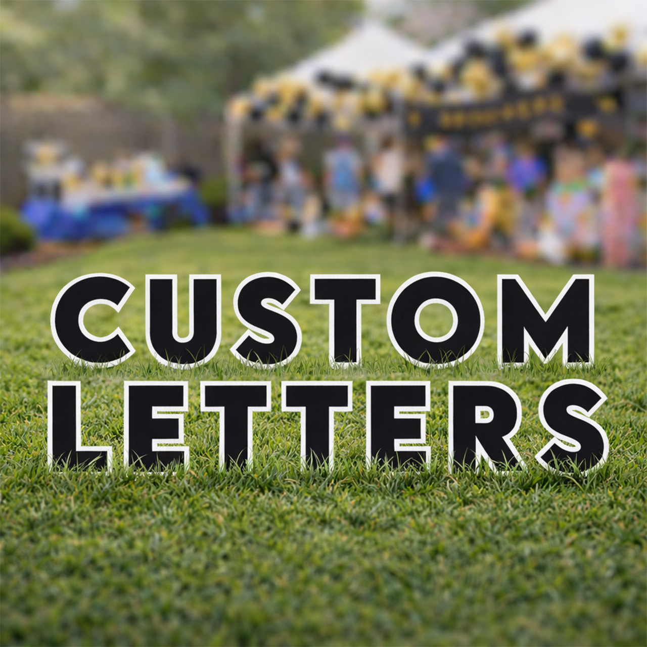 Black yard letters reading "CUSTOM LETTERS" with a white outline, standing on grass in front of a blurred backyard party scene with a white tent and yellow and black balloon decorations.