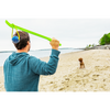 Dog owner joyfully using the Loop & Launch green launcher to toss the 3-inch orange ball to a playful dog in a sunny beach setting.