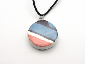 A round abstract red, white & blue ceramic pendant necklace. On a black cord necklace. A round abstract red, white & blue ceramic pendant necklace. On a black cord necklace.