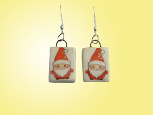A set of handcrafted ceramic dangle earrings with Santa's face on white rectangles. With a yellow background. A set of handcrafted ceramic dangle earrings with Santa's face on white rectangles. With a yellow background.