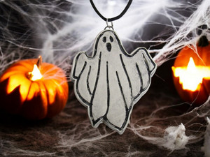 A handmade ceramic ghost statement pendant necklace. On a black cord necklace. With Halloween pumpkins and spider web look background. A handmade ceramic ghost statement pendant necklace. On a black cord necklace. With Halloween pumpkins and spider web look background.