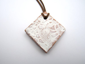 An aromatherapy terracotta diamond shaped white lace ceramic handmade necklace. On a brown cord necklace. An aromatherapy terracotta diamond shaped white lace ceramic handmade necklace. On a brown cord necklace.