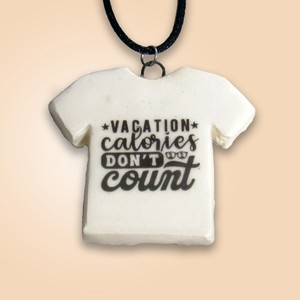 A ceramic Tshirt pendant with the words "Vacation Calories Don't Count". On a black cord necklace. With a light orange background. A ceramic Tshirt pendant with the words "Vacation Calories Don't Count". On a black cord necklace. With a light orange background.