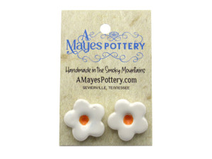 A set of handmade Large 5 petal Flowers (white flowers with orange centers) ceramic clay post earrings. On an A Mayes Pottery card. With a wood look background. A set of handmade Large 5 petal Flowers (white flowers with orange centers) ceramic clay post earrings. On an A Mayes Pottery card. With a wood look background.