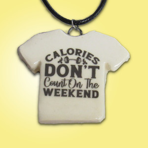 A handmade ceramic Tshirt pendant necklace with the words "Calories don't count on the weekend." On a black cord necklace. With a yellow background. A handmade ceramic Tshirt pendant necklace with the words "Calories don't count on the weekend." On a black cord necklace. With a yellow background.