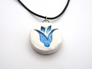 A handmade white with a blue tulip ceramic pendant necklace. On a black cord necklace. A handmade white with a blue tulip ceramic pendant necklace. On a black cord necklace.