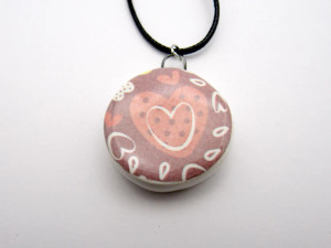 A ceramic round heart design pendant necklace. On a black cord necklace. A ceramic round heart design pendant necklace. A ceramic round heart design pendant necklace. On a black cord necklace. A ceramic round heart design pendant necklace.