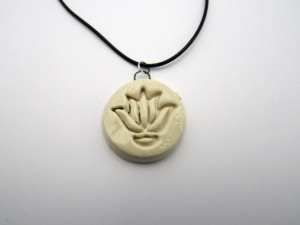A cream color abstract lotus flower round pendant on a black cord necklace. A cream color abstract lotus flower round pendant on a black cord necklace.