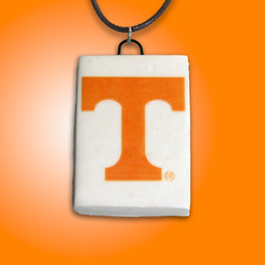 A TN Vols Power T rectangle handcrafted ceramic pendant. Pendant has a white background with the Orange Power T in the middle. With a black cord necklace. On an orange background. A TN Vols Power T rectangle handcrafted ceramic pendant. Pendant has a white background with the Orange Power T in the middle. With a black cord necklace. On an orange background.
