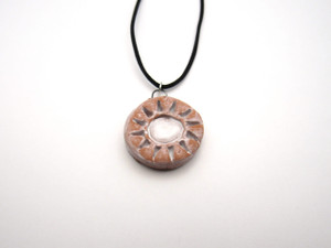 A handmade Abstract Sun Terracotta Pendant Necklace. The sun and sun rays are painted white.   With a black cord necklace. Made in America. In a laying position. A handmade Abstract Sun Terracotta Pendant Necklace. The sun and sun rays are painted white.   With a black cord necklace. Made in America. In a laying position.