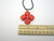 A solid red 4 pointed petal Flower shaped ceramic pendant necklace. On a black cord necklace. With ruler. Pendant measuring  approximately 1.5 inches wide.
