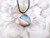 A round abstract red, white & blue ceramic pendant necklace. On a black cord necklace. With a white floral look background. A round abstract red, white & blue ceramic pendant necklace. On a black cord necklace. With a white floral look background.