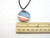 A round abstract red, white & blue ceramic pendant necklace. On a black cord necklace. With a ruler. Measuring approximately 1 inch wide. A round abstract red, white & blue ceramic pendant necklace. On a black cord necklace. With a ruler. Measuring approximately 1 inch wide.