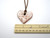 An aromatherapy heart shaped pendant terracotta diffuser for essential oils. On a brown cord necklace. With ruler. Pendant measuring approximately 2 inches wide.