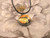 A ceramic round abstract pendant necklace, featuring fall colors. On a black cord necklace. With a floral look background.