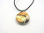 A ceramic round abstract pendant necklace, featuring fall colors. On a black cord necklace.