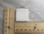 A plain white ceramic square pendant. With rulers. Measuring 1 inch by 1 inch.