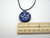 A handmade navy abstract 3 point design ceramic pendant necklace. On a black cord. With ruler. Measuring approximately 1 inch wide.
