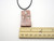 A leaves and stems (Design 1) ceramic Rectangle Terracotta pendant necklace. On a black cord necklace. With ruler. Measuring approximately 1 inch wide.