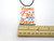 A Patriotic Ceramic Home of the Free Because of The Brave Infusion Statement Necklace. On a black cord necklace. With a ruler. Measuring approximately 1.5 inches wide.