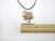 A Patriotic Flowers in Vase with Flag Infusion ceramic rectangle pendant on a black cord necklace. With ruler. Measuring approximately 1.5 inches wide.