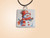 A handmade cute snowman with red hat and scarf ceramic pendant necklace. On a black cord necklace. With a light orange background. A handmade cute snowman with red hat and scarf ceramic pendant necklace. On a black cord necklace. With a light orange background.