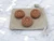 A set of 3 Aromatherapy stones terracotta clay essential oil diffusers. Stones have a flower design on them. Laying on top of a small cotton drawstring bag. With a gray marble background.