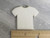 A plain white handmade ceramic Tshirt pendant. With ruler. Measuring approximately 1 inch wide at the bottom of the pendant.
