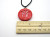 A handmade red tulip ceramic pendant necklace. On a black cord necklace. With a ruler. Measuring  approximately 1 inch wide.