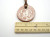 A handmade aromatherapy white flower design terracotta pendant necklace. On a brown cord necklace. With ruler. Measuring approximately 1.5 inches wide.