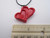 A handmade red double heart ceramic pendant necklace. On a black cord necklace. Shown with ruler. Measuring approximately 1 inch wide.