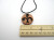 A handmade abstract (Flourish 1) round terracotta pendant necklace. Flourish design is painted black. On a black cord. With ruler. Measuring approximately 1 inch wide. A handmade abstract (Flourish 1) round terracotta pendant necklace. Flourish design is painted black. On a black cord. With ruler. Measuring approximately 1 inch wide.