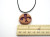 A handmade abstract (Flourish 1) round terracotta pendant necklace. Flourish design is painted purple.  On a black cord. With ruler. Measuring approximately 1 inch wide. A handmade abstract (Flourish 1) round terracotta pendant necklace. Flourish design is painted purple.  On a black cord. With ruler. Measuring approximately 1 inch wide.