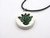 A white background and dark green abstract lotus flower round pendant on a black cord necklace.