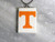 A TN Vols Power T rectangle handcrafted ceramic pendant. Pendant has a white background with the Orange Power T in the middle. With a black cord necklace. On a gray marble look background.