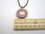 A handmade Abstract Sun Terracotta Pendant Necklace. The sun and sun rays are painted white.   With a black cord necklace. Made in America. In a laying position. Shown with ruler. A handmade Abstract Sun Terracotta Pendant Necklace. The sun and sun rays are painted white.   With a black cord necklace. Made in America. In a laying position. Shown with ruler.