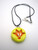 An Abstract Flower handmade pottery jewelry Ceramic necklace. Shown in yellow with an orange flower. On a black corded necklace. An Abstract Flower handmade pottery jewelry Ceramic necklace. Shown in yellow with an orange flower. On a black corded necklace.
