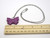 A Purple Ceramic Butterfly Pendant Necklace Handmade from fired earthenware clay. On a silver colored chain necklace. With ruler. Measuring approximately 1.25 inches long. A Purple Ceramic Butterfly Pendant Necklace Handmade from fired earthenware clay. On a silver colored chain necklace. With ruler. Measuring approximately 1.25 inches long.