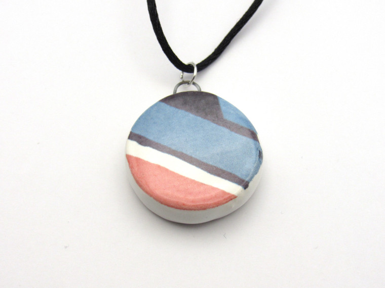 A round abstract red, white & blue ceramic pendant necklace. On a black cord necklace.