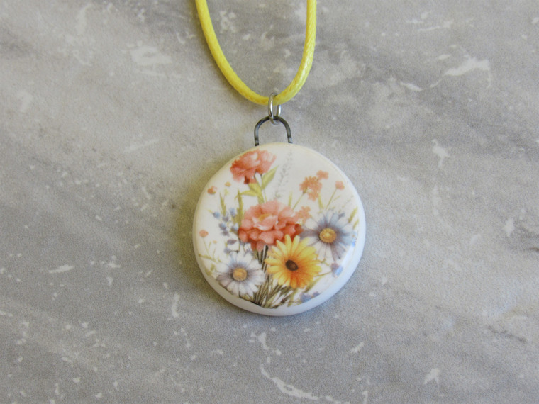 A handmade Beautiful Bundle Mixed Flowers round ceramic pendant necklace. On a yellow cord necklace.