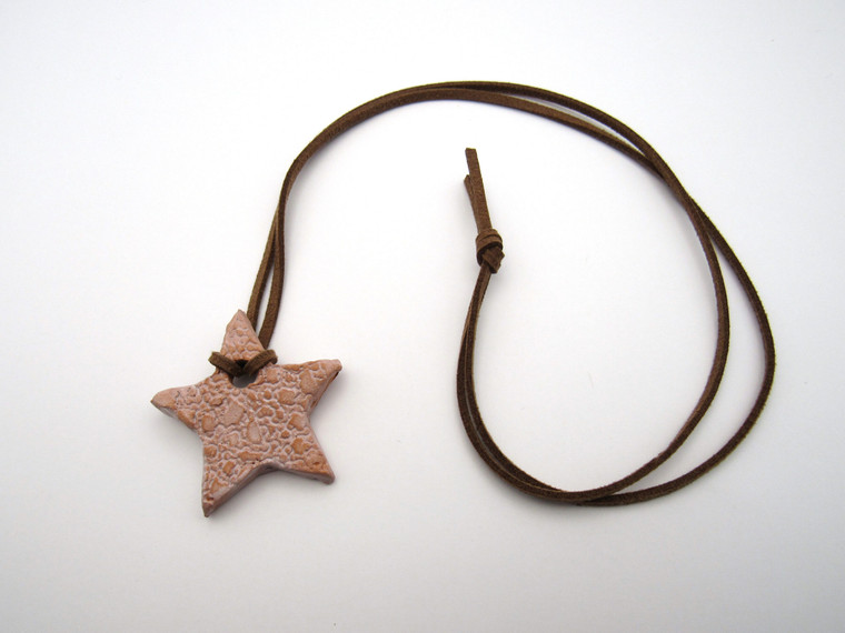 An aromatherapy small star shaped pendant-terracotta diffuser for essential oils. On cord necklace. In a laying position.