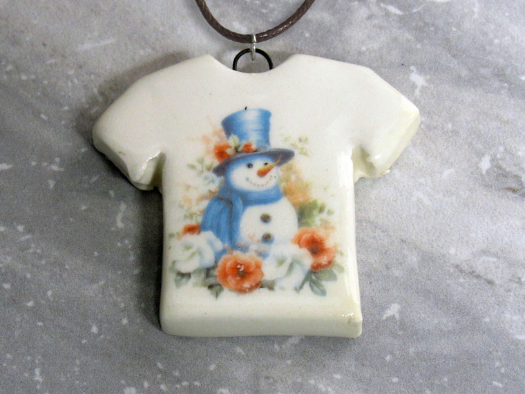 A handmade snowman with Blue Hat and scarf ceramic pendant necklace. On a black cord necklace. With a gray marble look background.